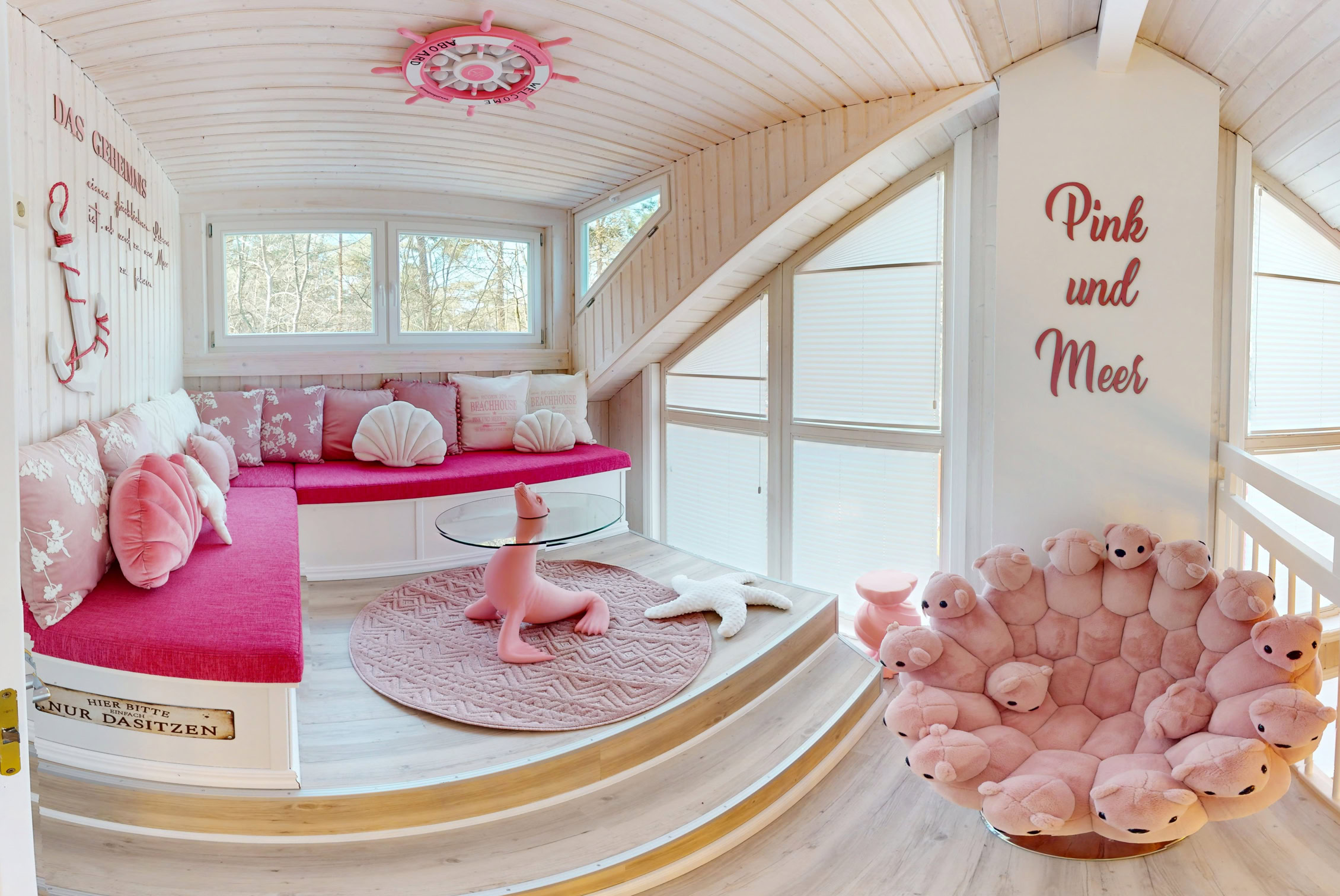 Ein Raum mit pink und weißen Möbeln, darunter ein Sofa mit Kissen, ein runder Teppich, ein dekorativer Stuhl und ein Spielzeugpferd. An der Wand steht "Pink and Mint".