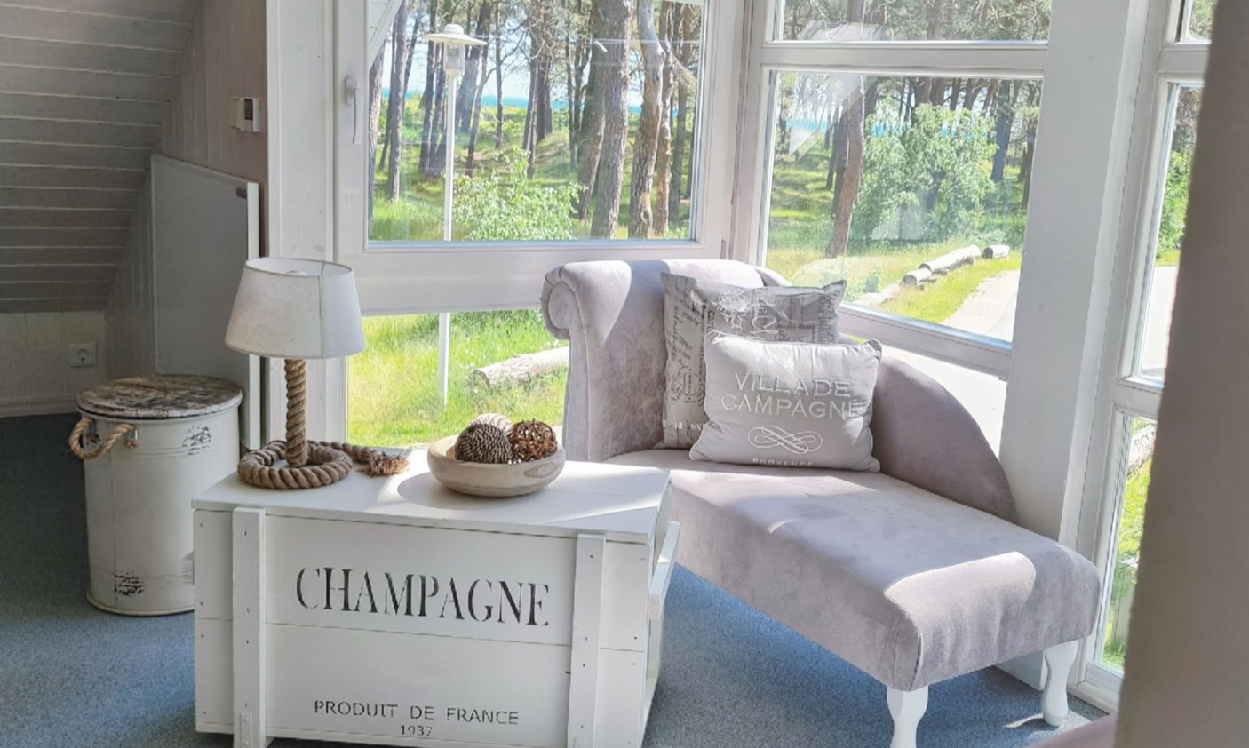 Gemütlicher Raum mit einem hellen Sessel, einem kleinen Tisch mit der Aufschrift "Champagne" und einem Fenster mit Blick auf Bäume.