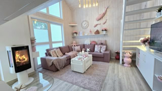 Gemütliches Wohnzimmer mit einem Ecksofa, Couchtisch, Kamin, Treppe und dekorativen Elementen in Rosa- und Beigetönen.