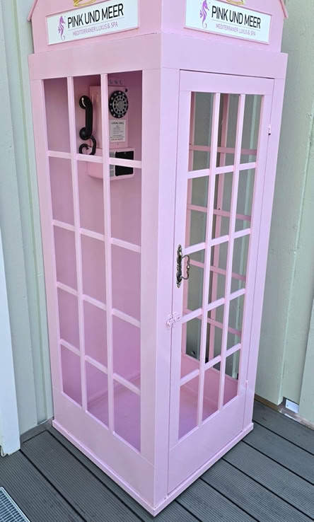 Rosa Telefonzelle mit Glasfenstern und einem Schild mit der Aufschrift "Telefonzelle" oben.